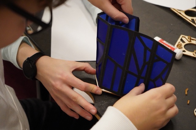a lantern in progress, hands are holding blue lasered lantern parts that are about to be put togehter